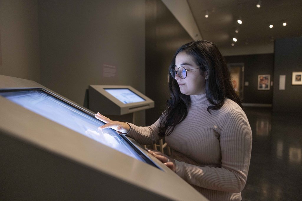 A woman engages with a digital interactive screen within the gallery.