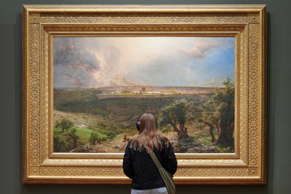 An image of a woman standing in front of a landscape painting