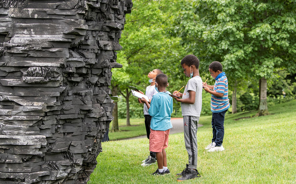 four school children take notes in front of a sculpture in the Sculpture Park