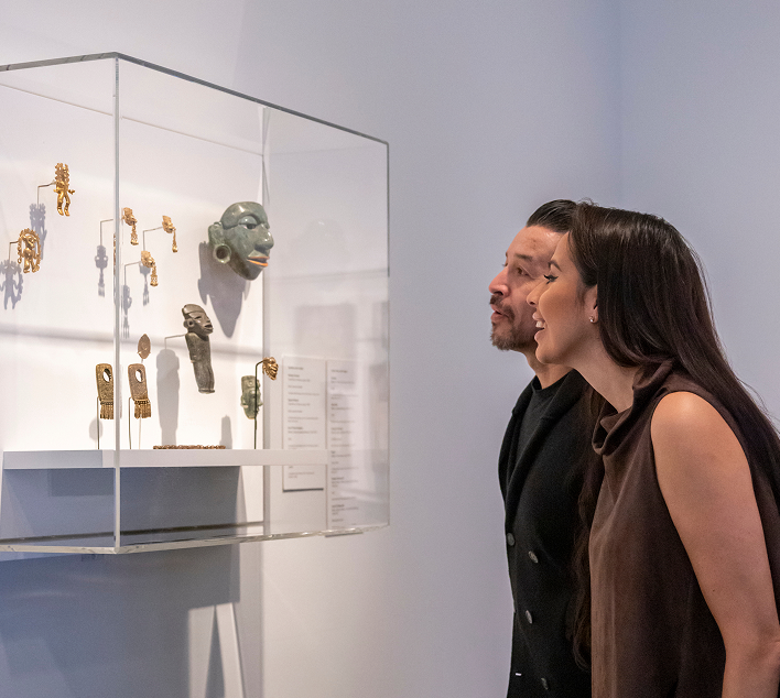 Two guests examine case of mesoamerican artifacts.