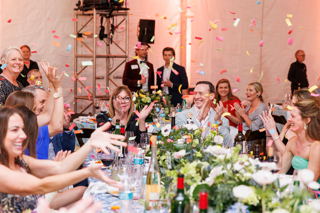 A group of people seated and clapping at a table as confetti flies around