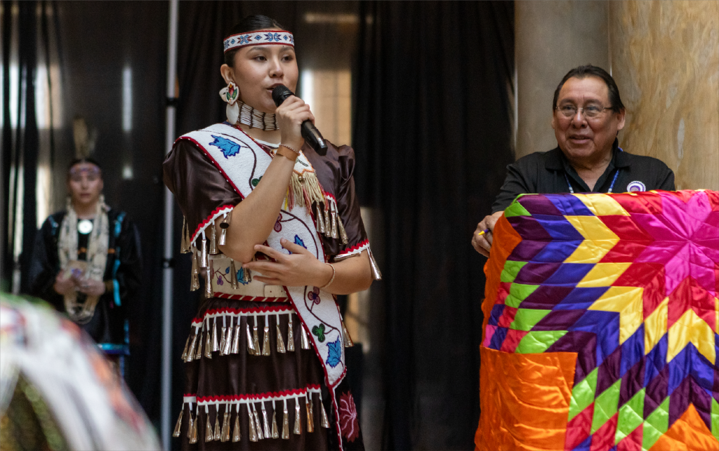 A person talks into a mic with a colorful quilt in the background