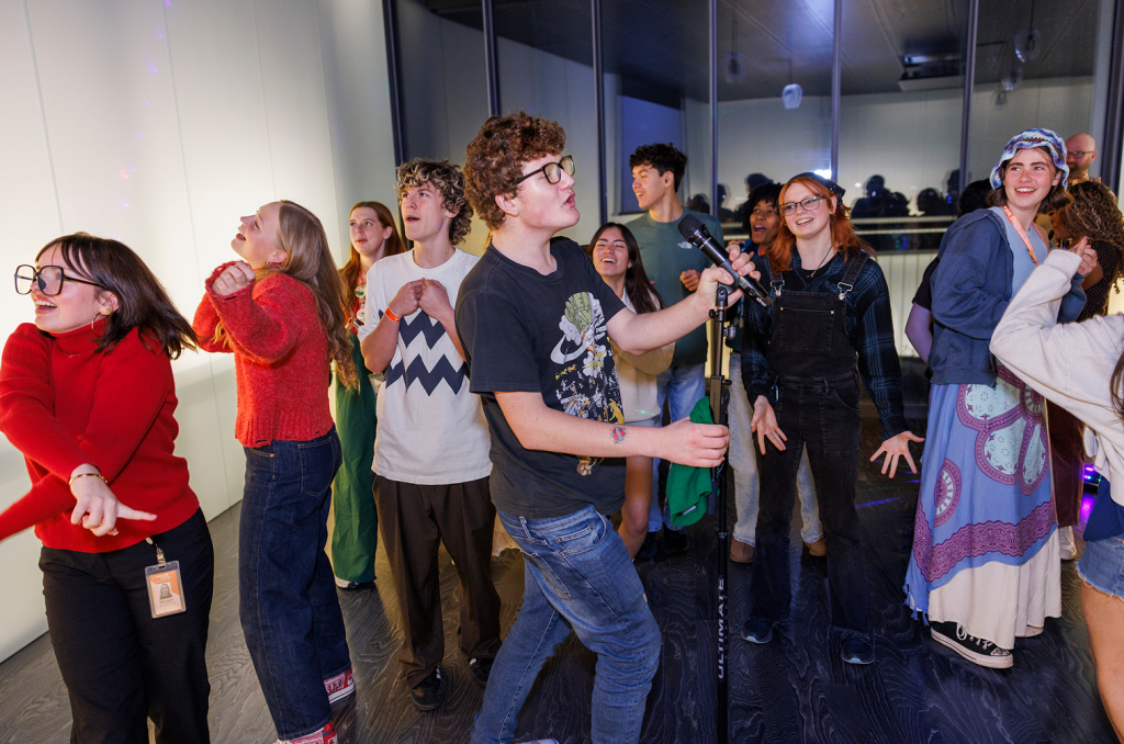 A group of teens singing and dancing around a microphone