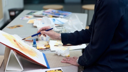 Multiple colors of pain on a table with pant brushes in them.