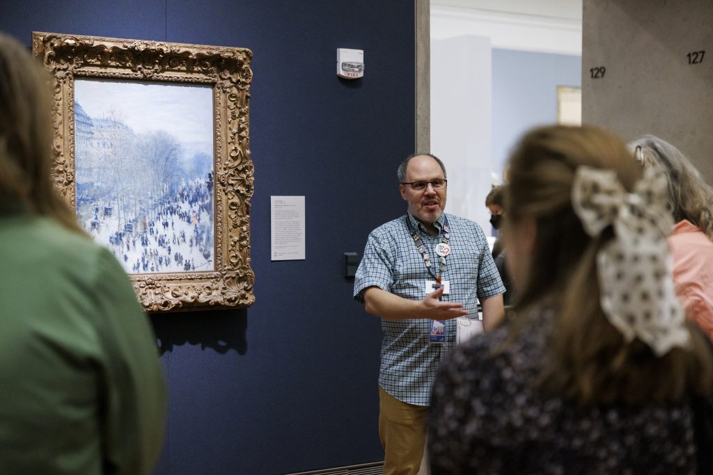 A museum tour guide stands in front of an impressionist painting
